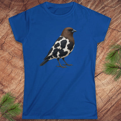 A royal blue short-sleeve crewneck t-shirt featuring a graphic of a black and white speckled bird with a brown head, laid flat on a textured wood background with pine needles in the corners.