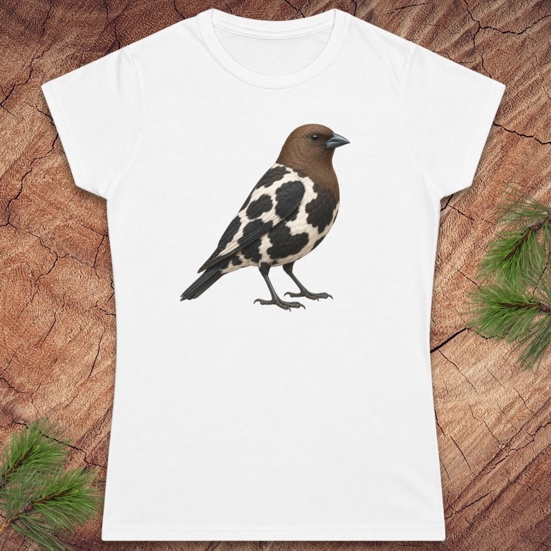 A white short-sleeve crewneck t-shirt featuring a detailed graphic of a brown and black-and-white speckled bird, laid flat on a textured brown wood background with pine needles in the corners.