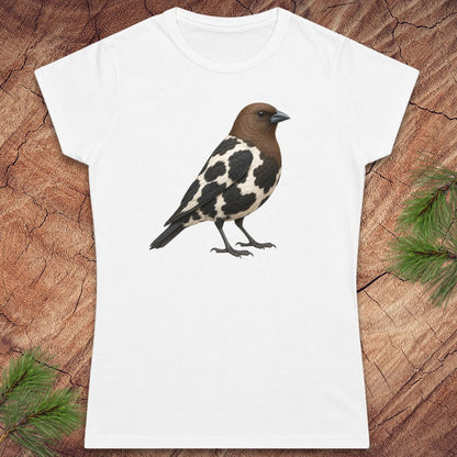 A white short-sleeve crewneck t-shirt featuring a detailed graphic of a brown and black-and-white speckled bird, laid flat on a textured brown wood background with pine needles in the corners.
