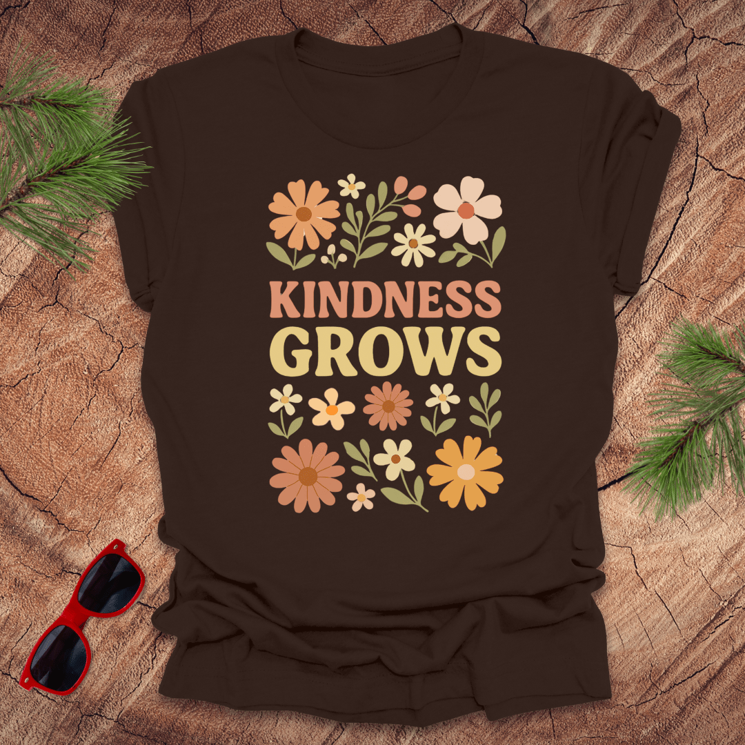 Brown t-shirt with flowers and text 'Kindness Grows' on a wood background.