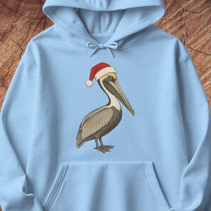 A light blue pullover hoodie laid flat on a textured brown wood background, featuring a printed illustration of a brown pelican wearing a red Santa hat with a white trim.