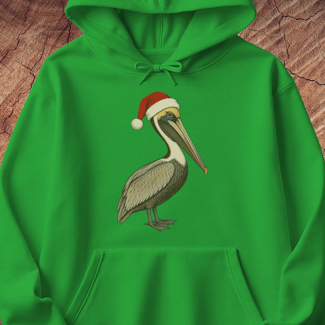 A bright green pullover hoodie laid flat on a textured brown wood background, featuring a printed illustration of a brown pelican wearing a red Santa hat on the chest.