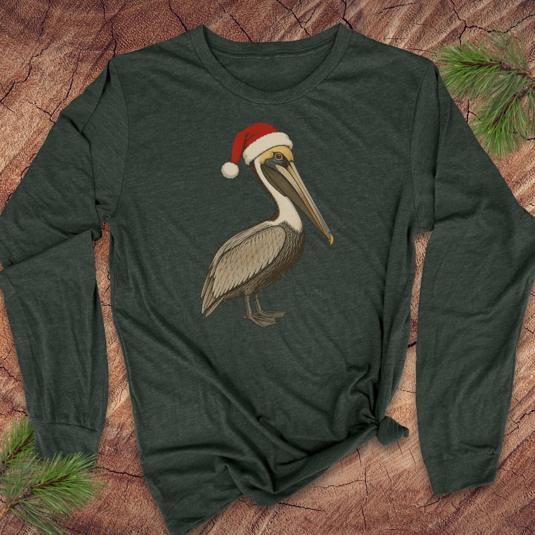 A dark heather green long-sleeve t-shirt featuring a graphic of a brown pelican wearing a red and white Santa hat, laid flat on a rustic wood background with pine branches.
