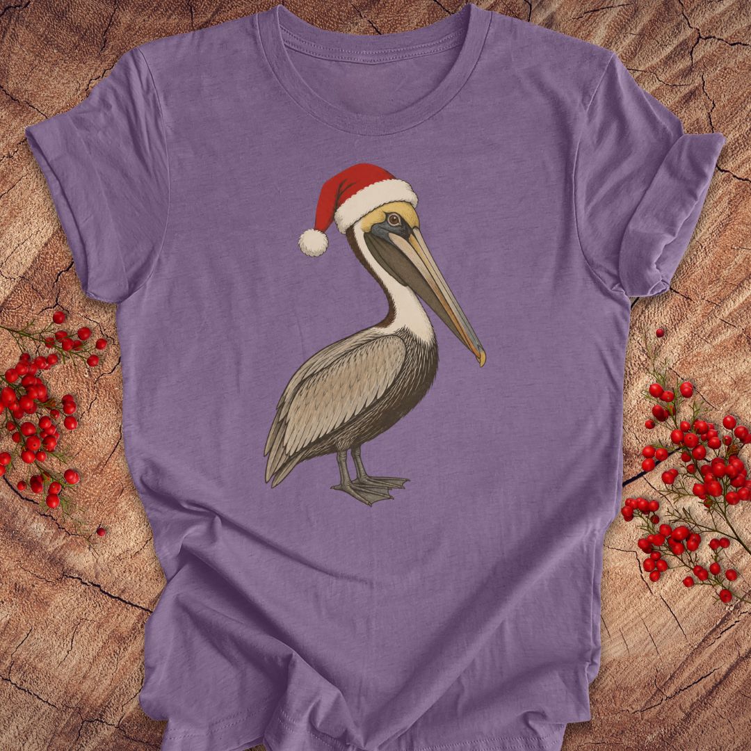 A purple short-sleeve t-shirt laid flat on a rustic wood background, featuring a graphic of a brown pelican wearing a red Santa hat. Red berry sprigs are placed on both sides of the shirt.