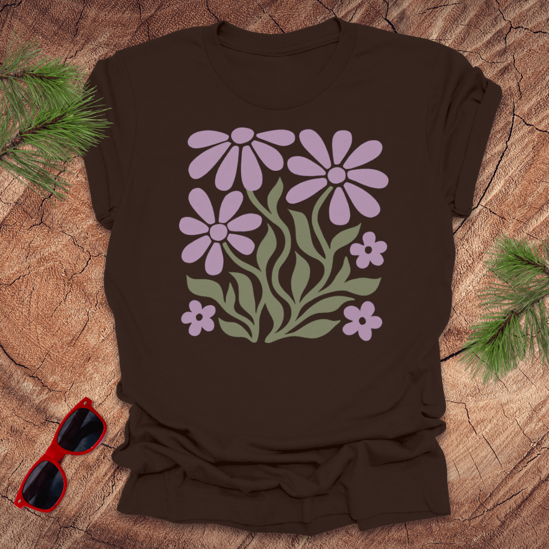 Brown t-shirt with purple floral design on a wooden surface with sunglasses and greenery.