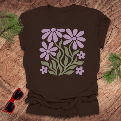 Brown t-shirt with purple floral design on a wooden surface with sunglasses and greenery.