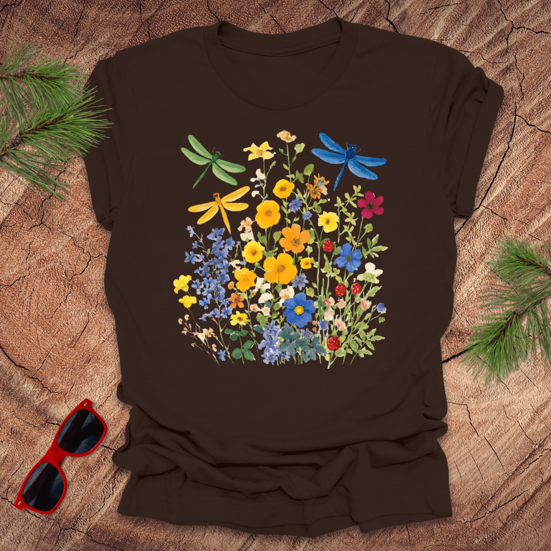 Brown t-shirt with floral and dragonfly design on a wooden surface with sunglasses and greenery.