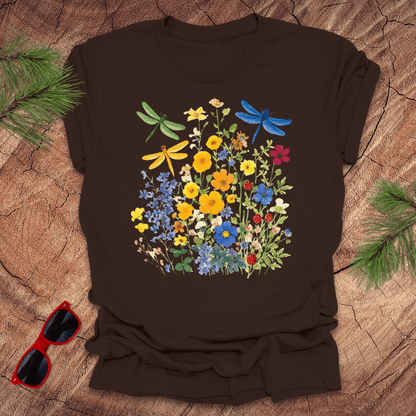 Brown t-shirt with floral and dragonfly design on a wooden surface with sunglasses and greenery.