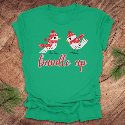 Green t-shirt with two birds with hats and scarves and text, 'Bundle up' on a wood background