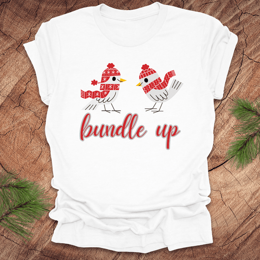 White t-shirt with two birds with hats and scarves and text, 'Bundle up' on a wood background
