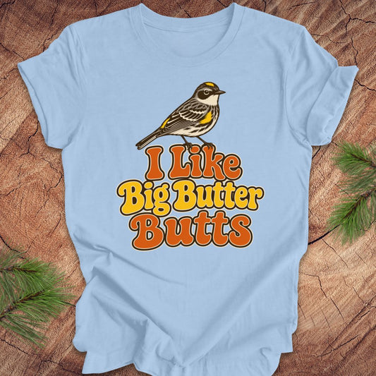 Light blue t-shirt with a bird graphic and text 'I Like Big Butter Butts' on a wooden surface.