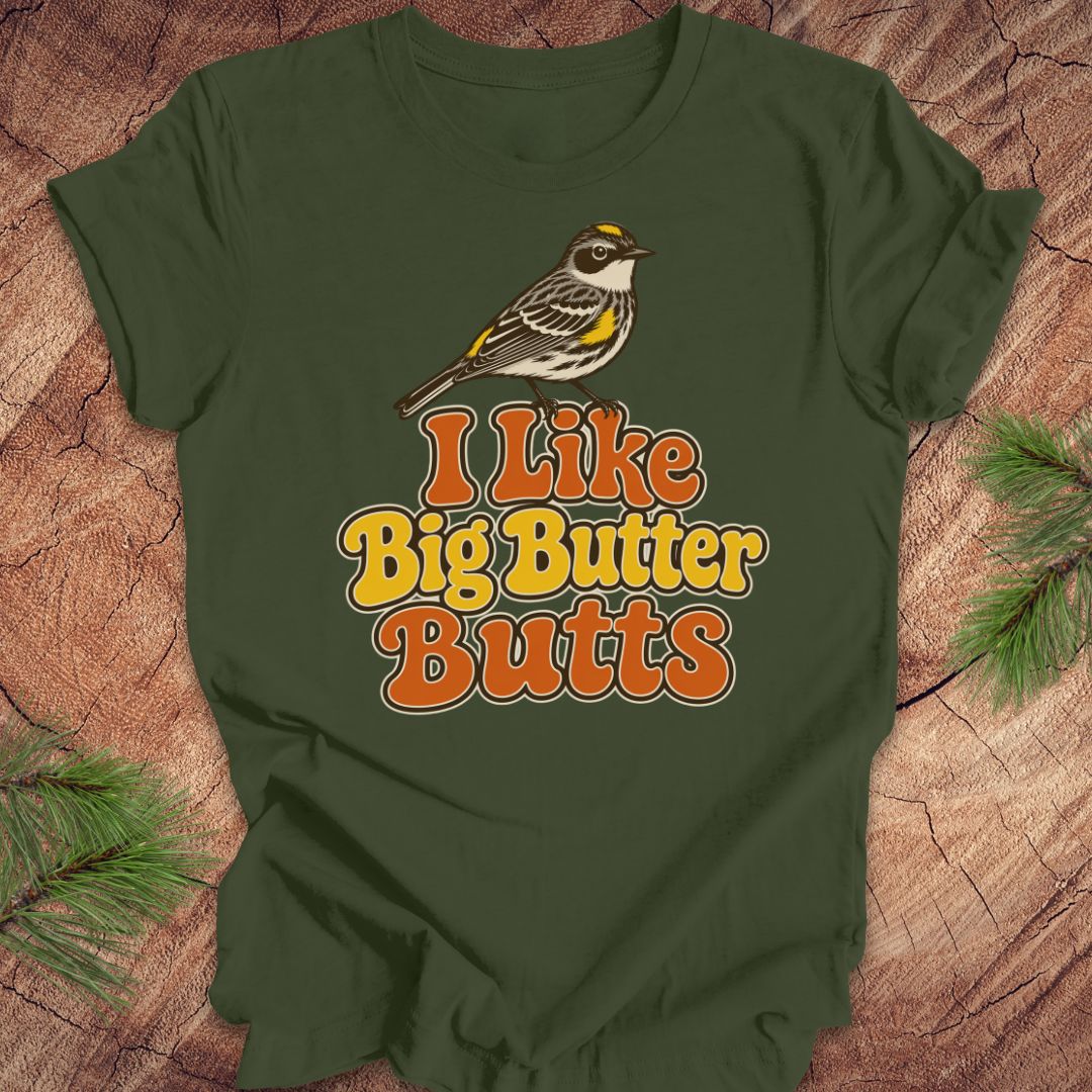 Green t-shirt with a bird graphic and text 'I Like Big Butter Butts' on a wooden surface.