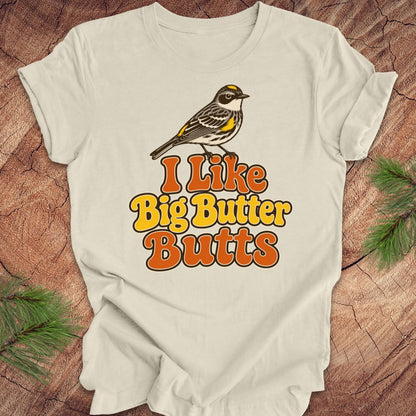Beige t-shirt with a bird graphic and text 'I Like Big Butter Butts' on a wooden surface.