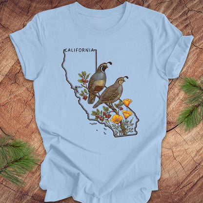 Light blue t-shirt with California design featuring quails and poppies on a wooden surface.