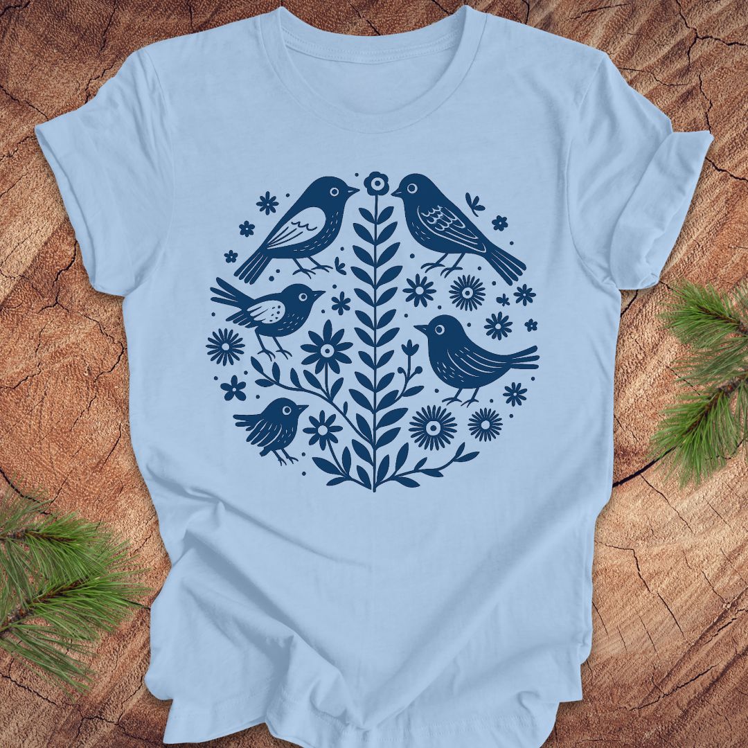 Baby blue t-shirt with folk art blue bird and floral design on a wooden surface