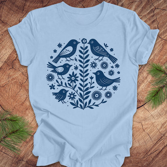 Baby blue t-shirt with folk art blue bird and floral design on a wooden surface