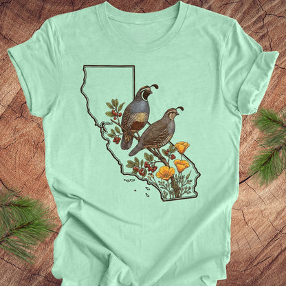 Light green t-shirt with a graphic of California, birds, and poppies on a wooden surface.