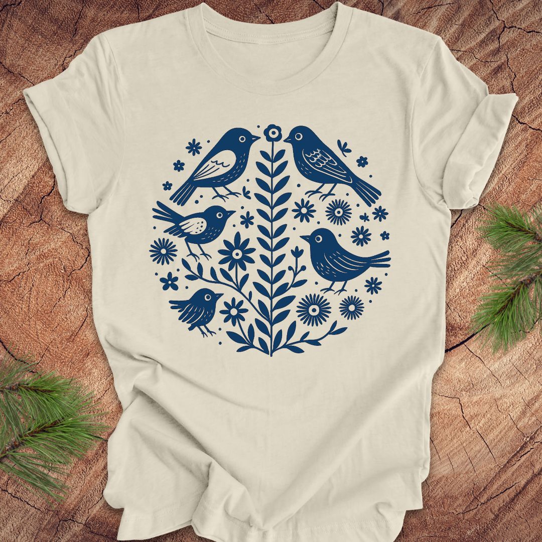 Beige t-shirt with folk art blue bird and floral design on a wooden surface