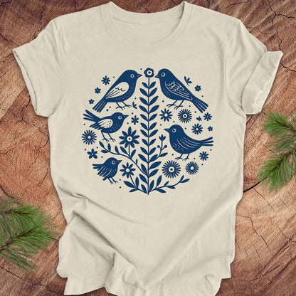 Beige t-shirt with folk art blue bird and floral design on a wooden surface
