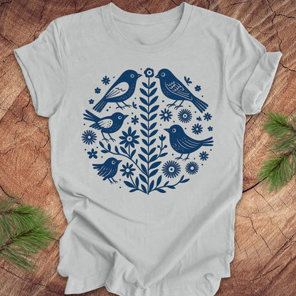 Silver t-shirt with folk art blue bird and floral design on a wooden surface