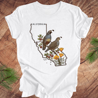 White t-shirt with California map design featuring quails and flowers on a wooden surface.