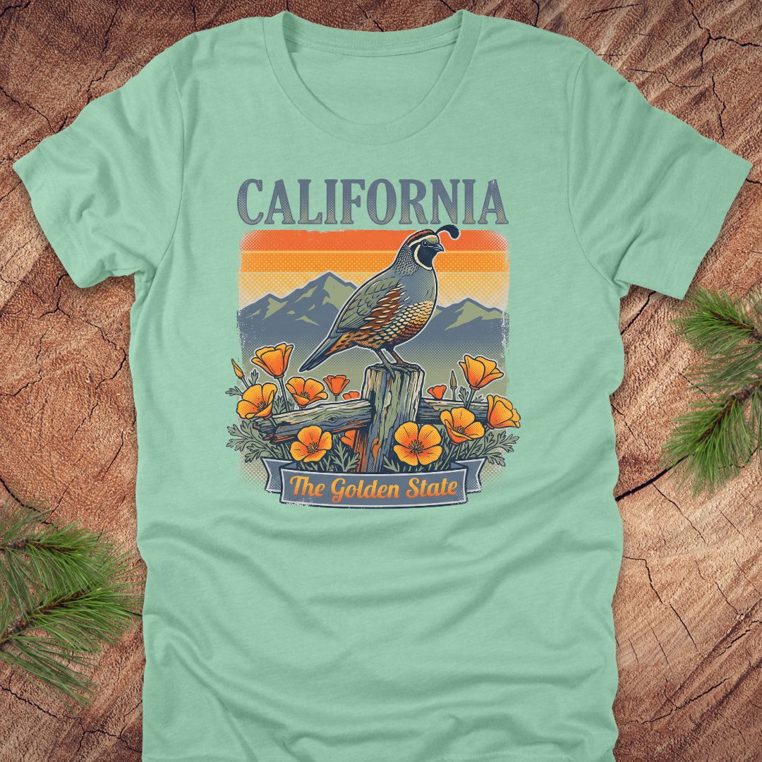 Light green t-shirt with California-themed graphic featuring a bird, mountains, and flowers on a wooden surface.