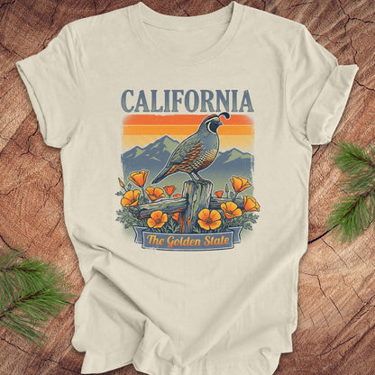 Beige t-shirt with California-themed design featuring a quail, mountains, and poppies on a wooden surface.
