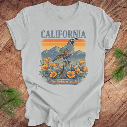 Gray t-shirt with California-themed design featuring a quail, mountains, and poppies on a wooden surface.
