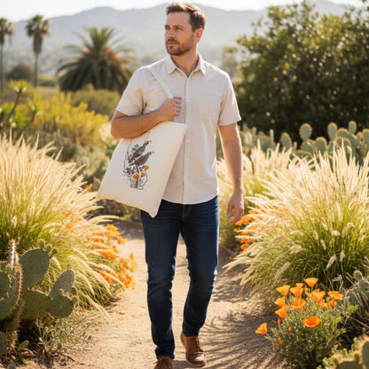 Man walking through a garden with plants and flowers, holding a California birds tote bag.