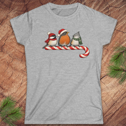 Sport grey women's t-shirt with a Black-capped Chickadee, American Robin, and Tufted Titmouse in winter hats and scarves perched on a candy cane, laid flat on a rustic wood background with pine branches.