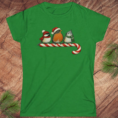 Irish green women's t-shirt with a Black-capped Chickadee, American Robin, and Tufted Titmouse in winter hats and scarves perched on a candy cane, laid flat on a rustic wood background with pine branches.
