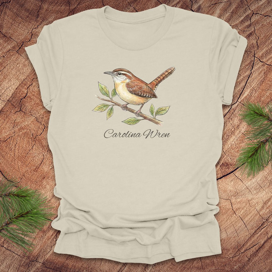 Beige t-shirt with a Carolina Wren illustration and text, 'carolina wren' on a wooden surface