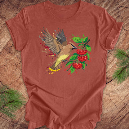 Clay colored t-shirt with a cedar waxwing bird and berry design on a wooden surface