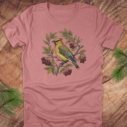 Mauve t-shirt with a cedar waxwing bird and leaf design on a wooden surface