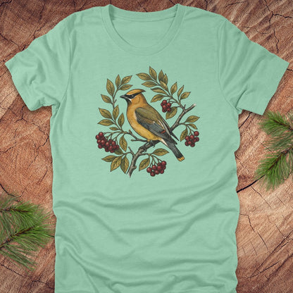 Mint green t-shirt with a cedar waxwing bird and leaf design on a wooden surface