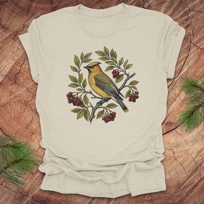 Beige t-shirt with a cedar waxwing bird and leaf design on a wooden surface