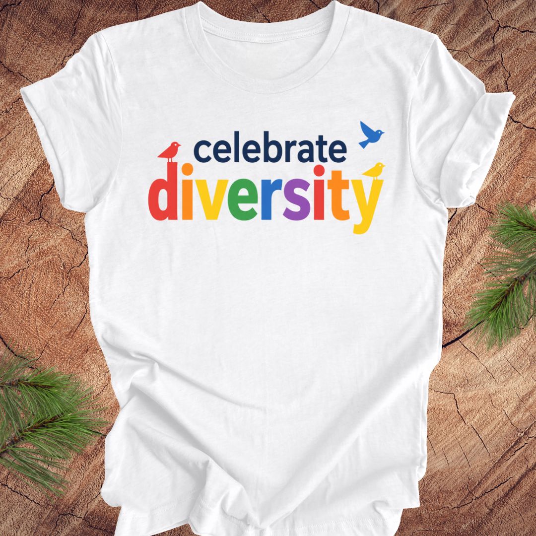 White t-shirt with 'celebrate diversity' text in colorful letters on a wooden surface.