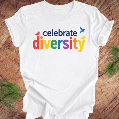 White t-shirt with 'celebrate diversity' text in colorful letters on a wooden surface.