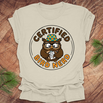 Beige t-shirt with a cartoon owl design and 'Certified Bird Nerd' text on a wooden surface.