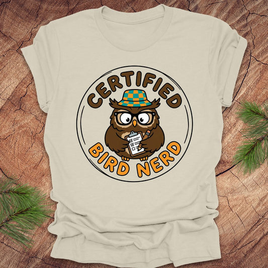 Beige t-shirt with a cartoon owl design and 'Certified Bird Nerd' text on a wooden surface.