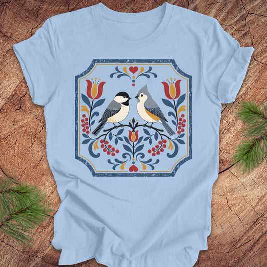 Light blue t-shirt with chickadee, titmouse and floral design on a wooden surface