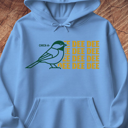 A light blue hoodie laid flat on a textured wood background, featuring a green chick-a-doodle bird graphic and the text 'CHICK-A-DEE-DEE' repeated in yellow on the chest.