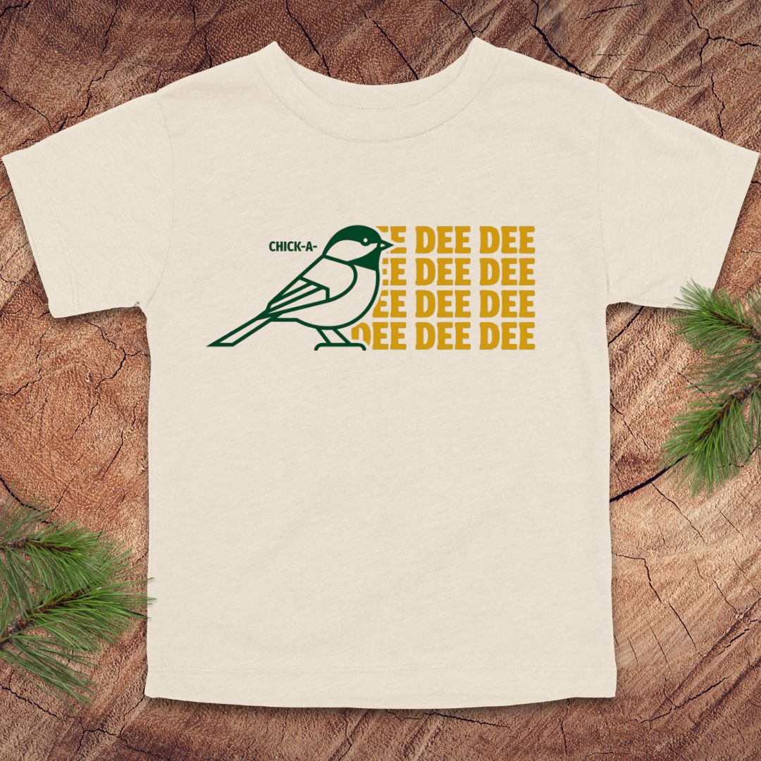 Beige toddler tshirt with a chickadee design and text on a wood background.