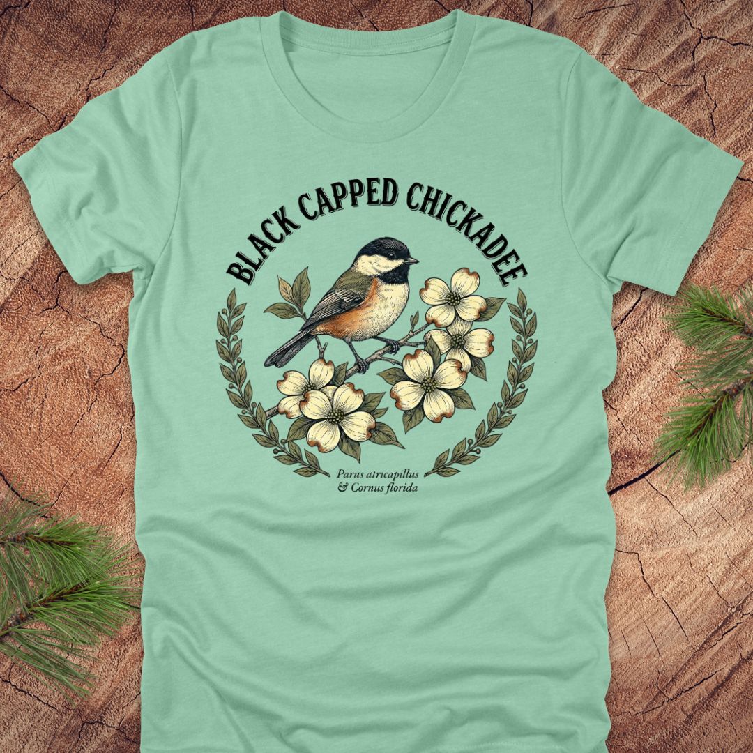 Light green t-shirt with black-capped chickadee design on a wooden surface