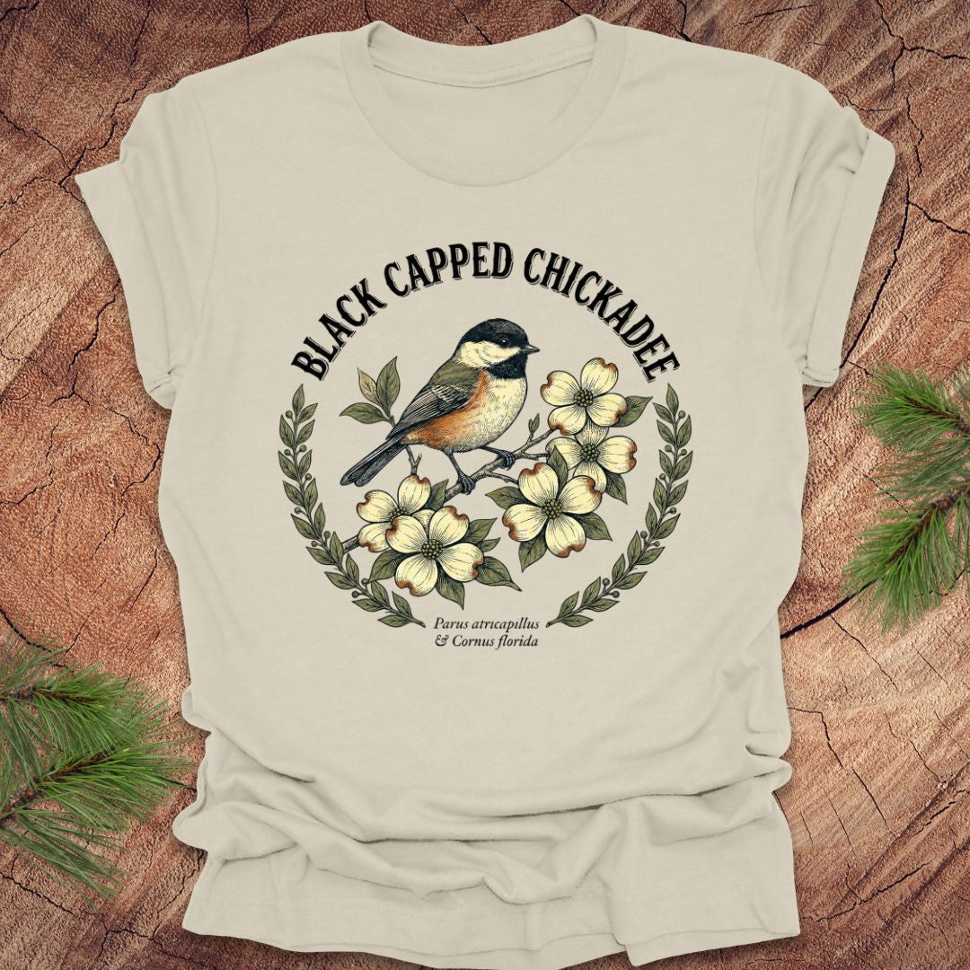 Beige t-shirt with black-capped chickadee design on a wooden surface
