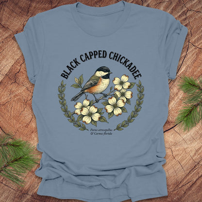 Blue t-shirt with a black-capped chickadee design on a wooden surface