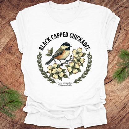 White t-shirt with black-capped chickadee design on a wooden surface