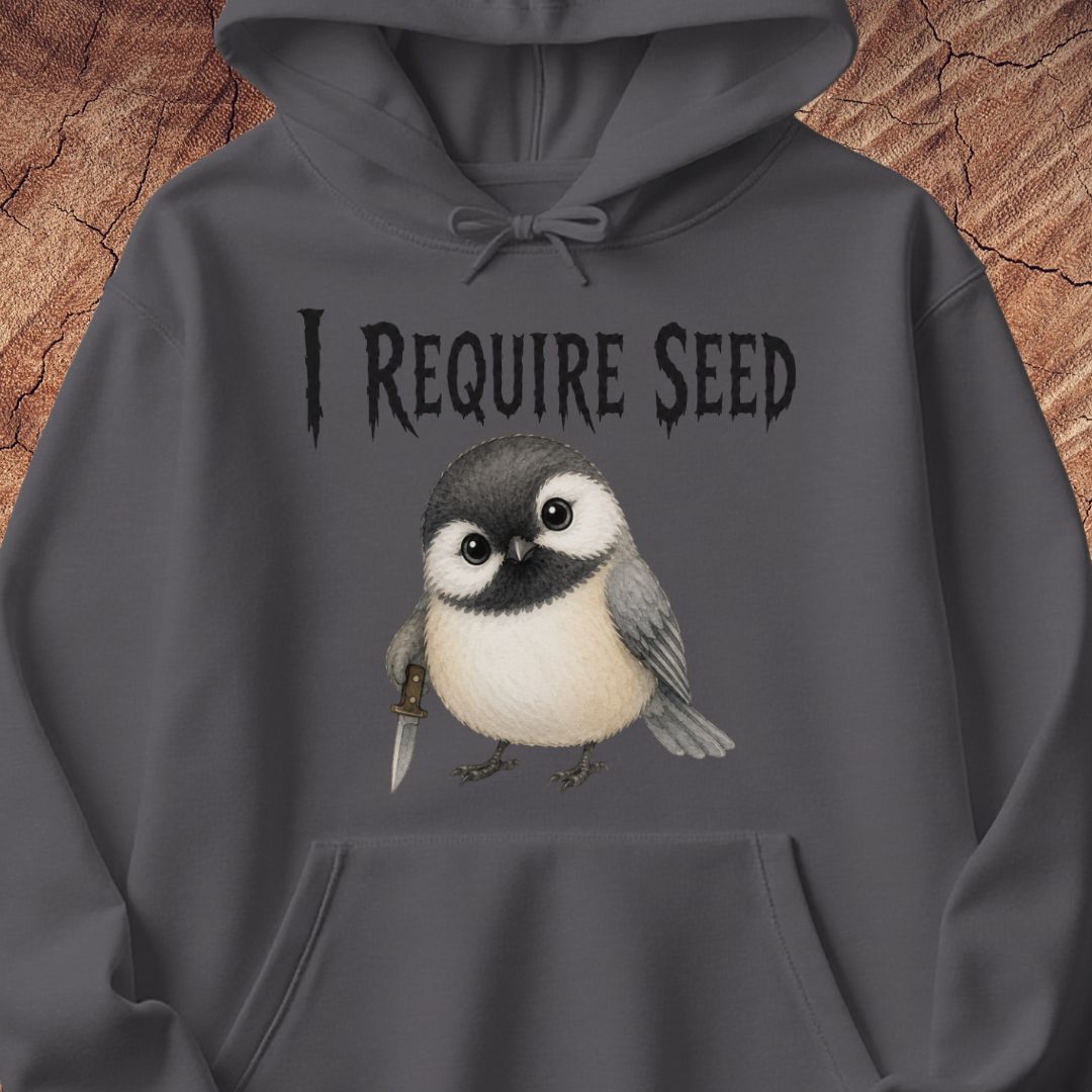 A dark gray hoodie featuring a graphic print of a small bird holding a knife with the text 'I REQUIRE SEED' above it, displayed against a rustic wood background.