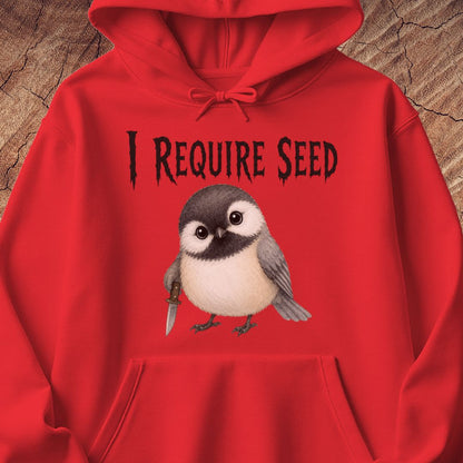 A bright red hoodie laid flat against a textured wood background, featuring a graphic print of a small bird holding a knife beneath the text 'I REQUIRE SEED' in a black stylized font.