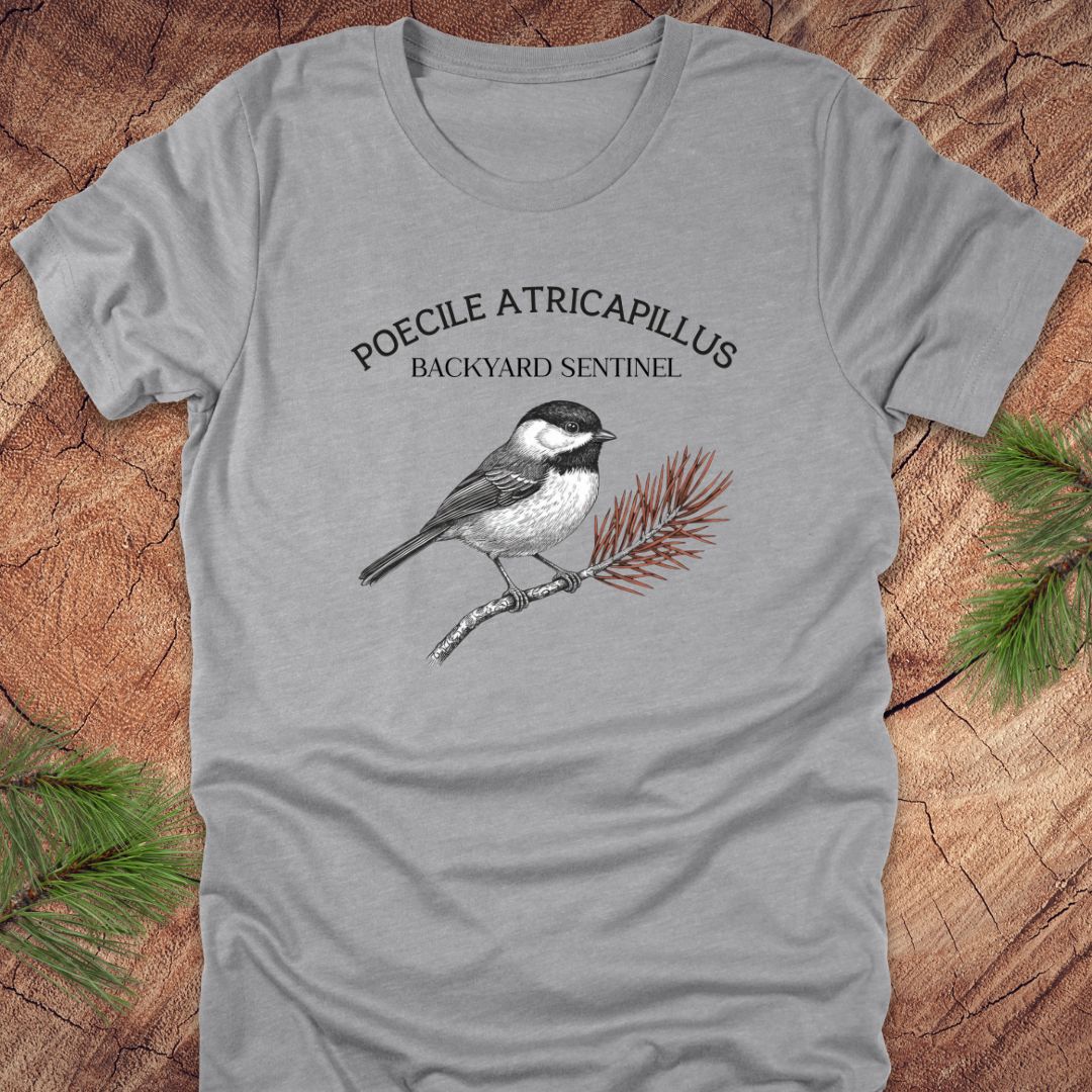 Gray t-shirt with a chickadee illustration and scientific name on a wooden surface
